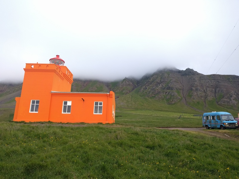 orange lighthouse with
endless mountains behind and also a rusted-out mess of a van